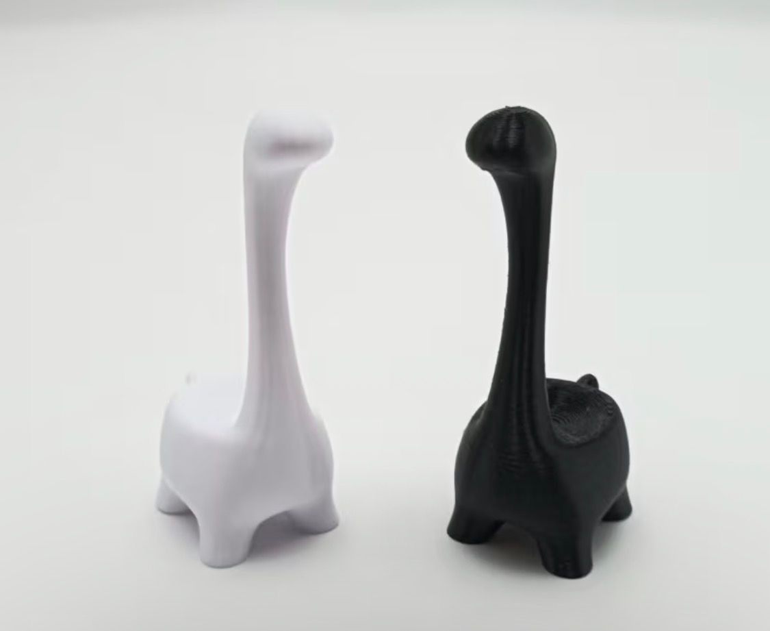 Two small dinosaur figurines, one white and one black, standing side by side on a light background