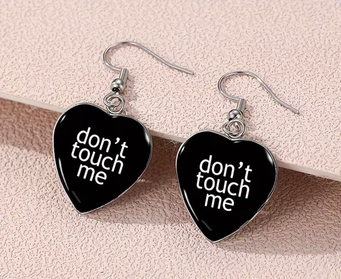 Black heart earrings with white text reading “don’t touch me” on silver hooks.