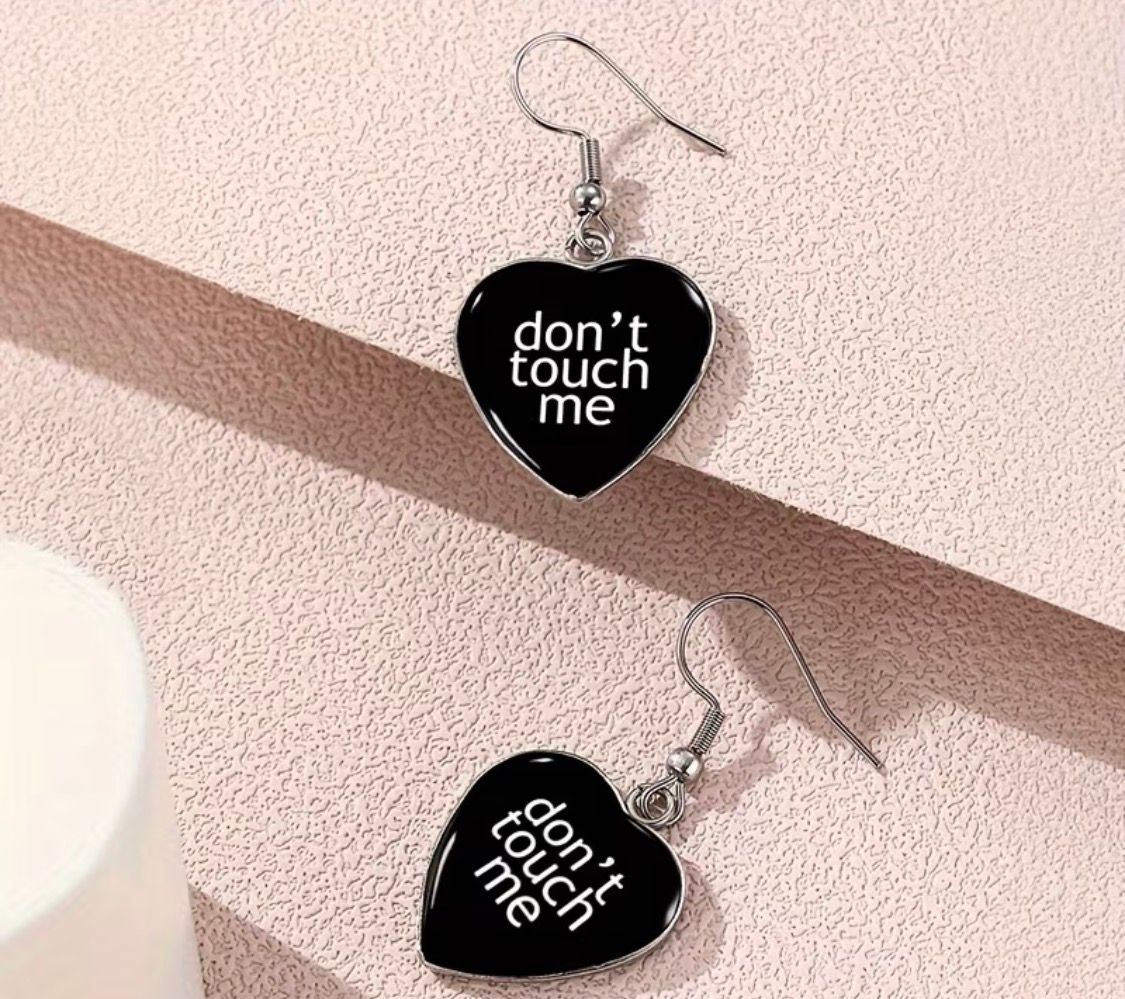 Black heart earrings with white text reading “don’t touch me” on silver hooks.