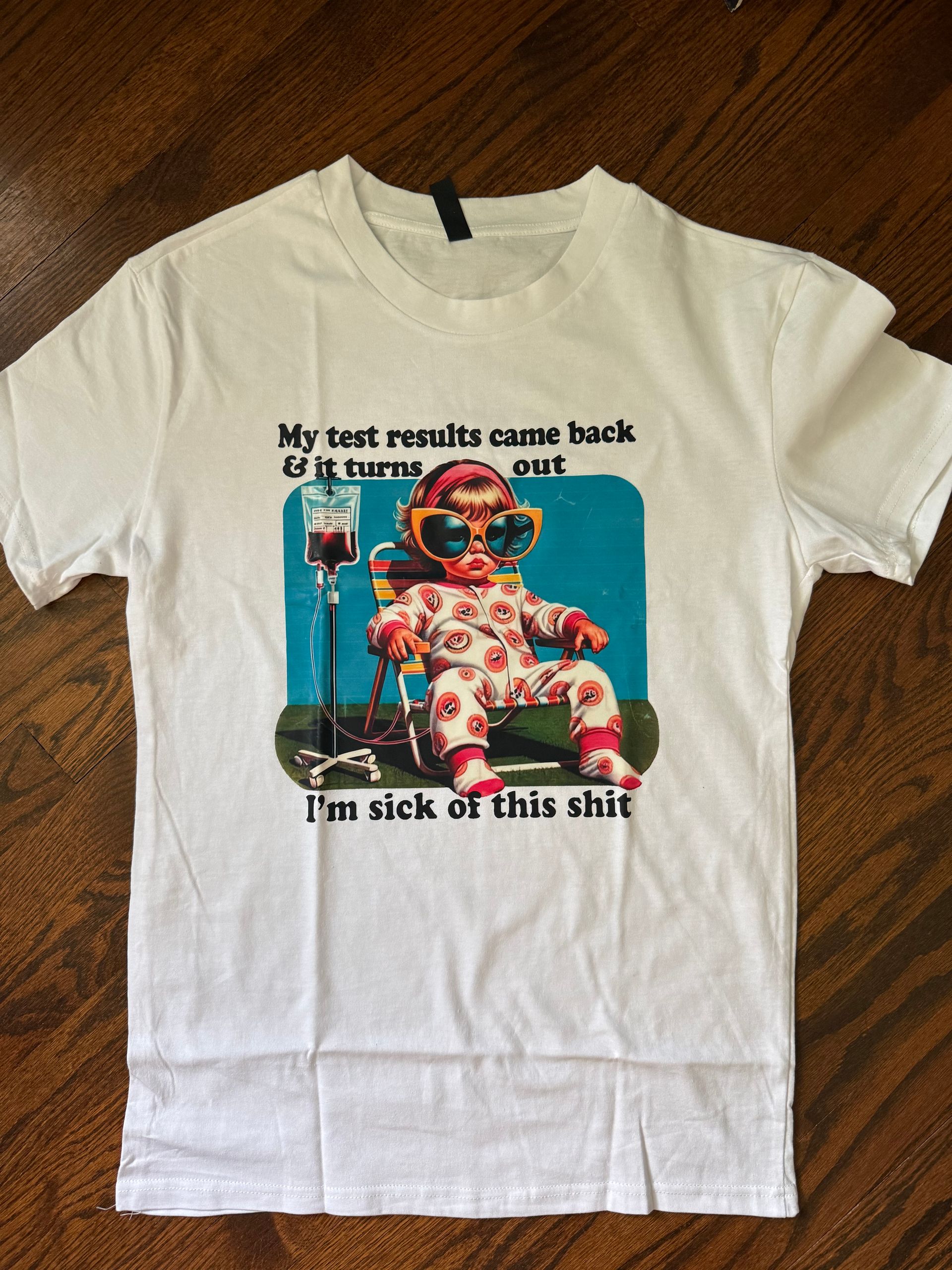 White T-shirt with a colorful graphic and bold text on a wooden floor.