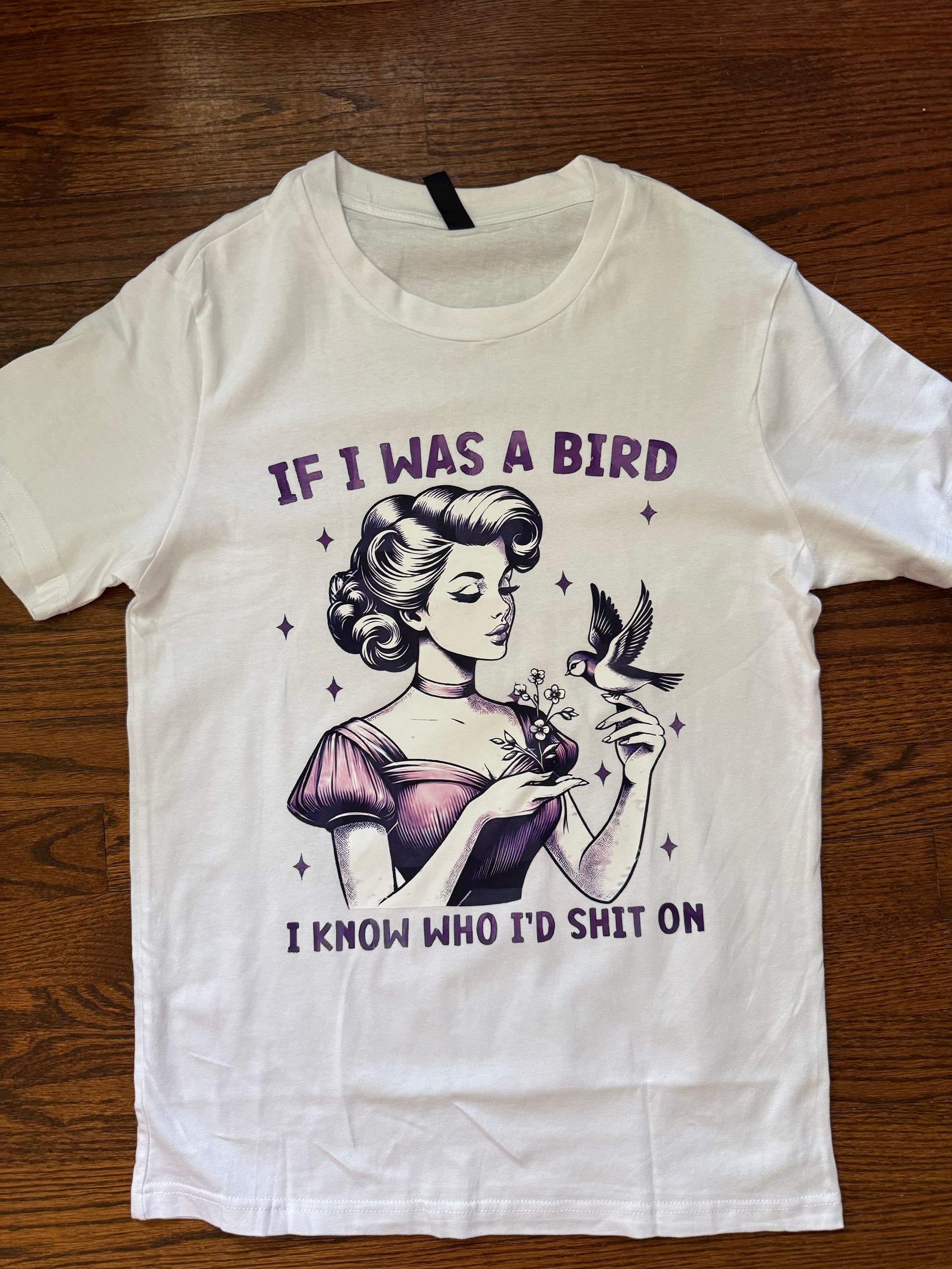 White T-shirt with a vintage-style bird and woman graphic and purple text reading, “IF I WAS A BIRD I KNOW WHO I’D SHIT ON.”