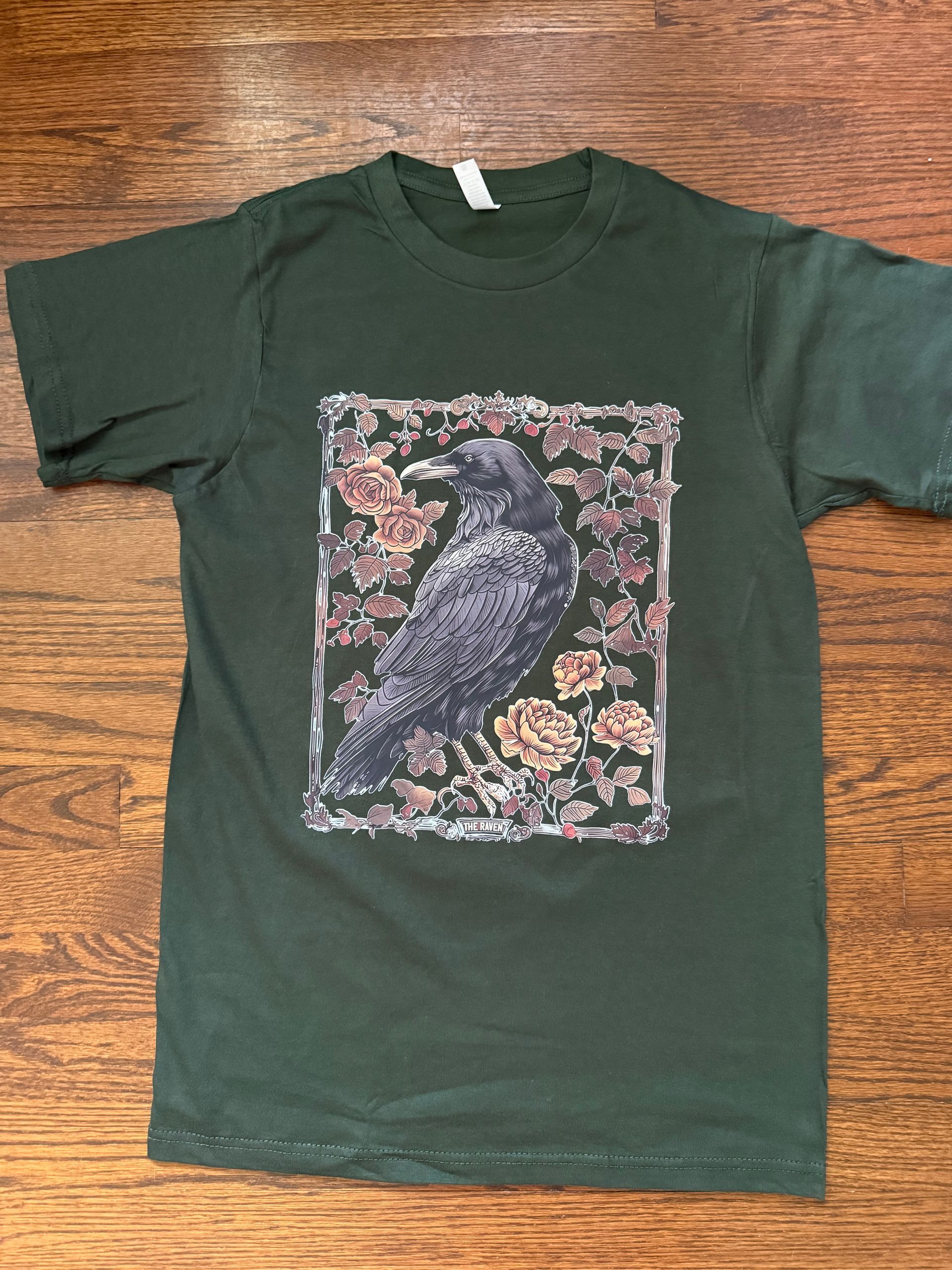 Dark green T-shirt with a floral-bordered raven graphic on the front.