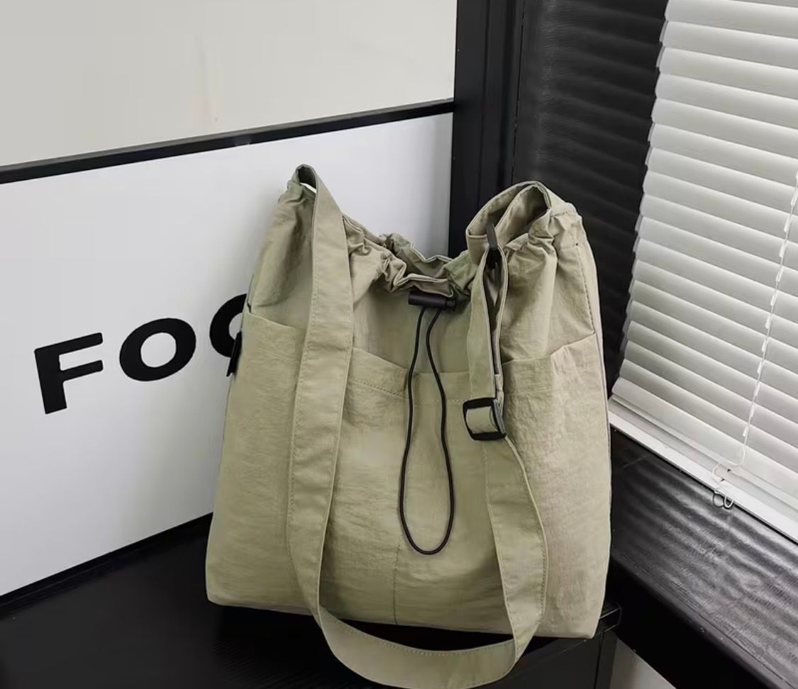 Beige drawstring tote bag on a table beside a white box and window blinds
