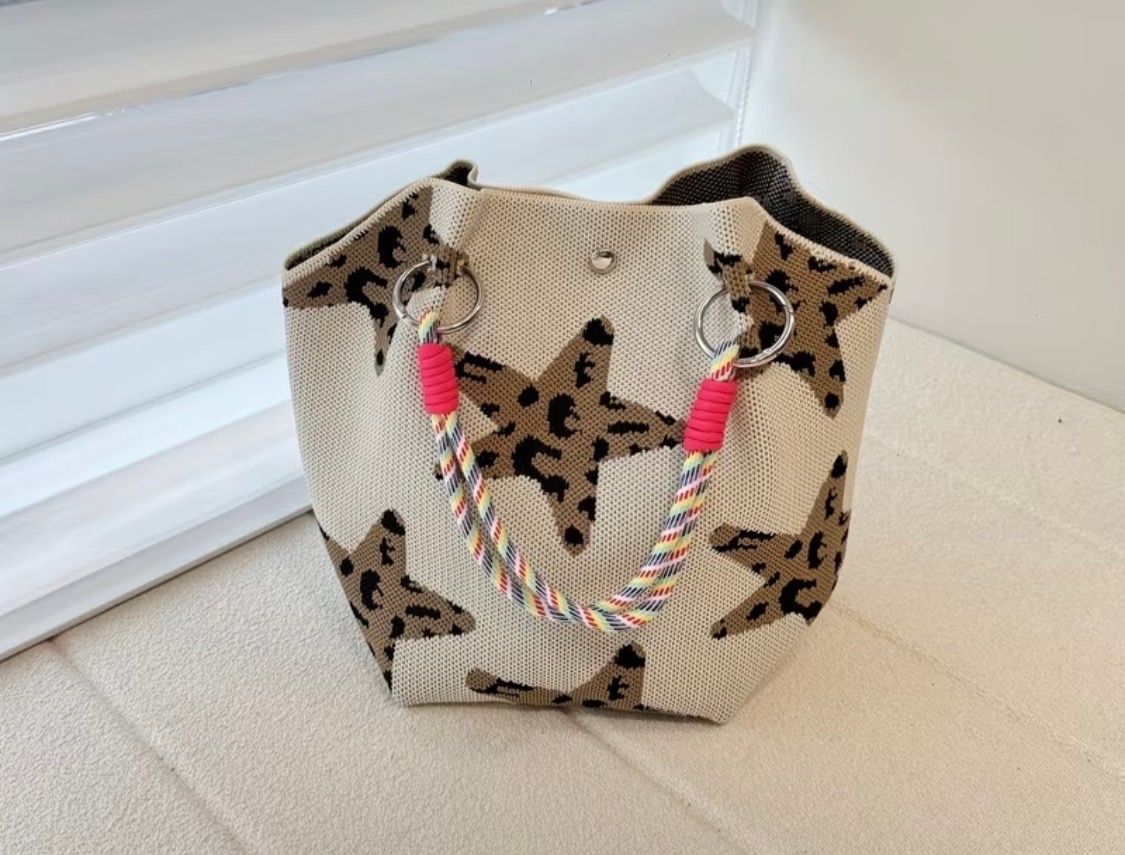 Leopard-print drawstring bag with blue beaded handles on a black leather chair