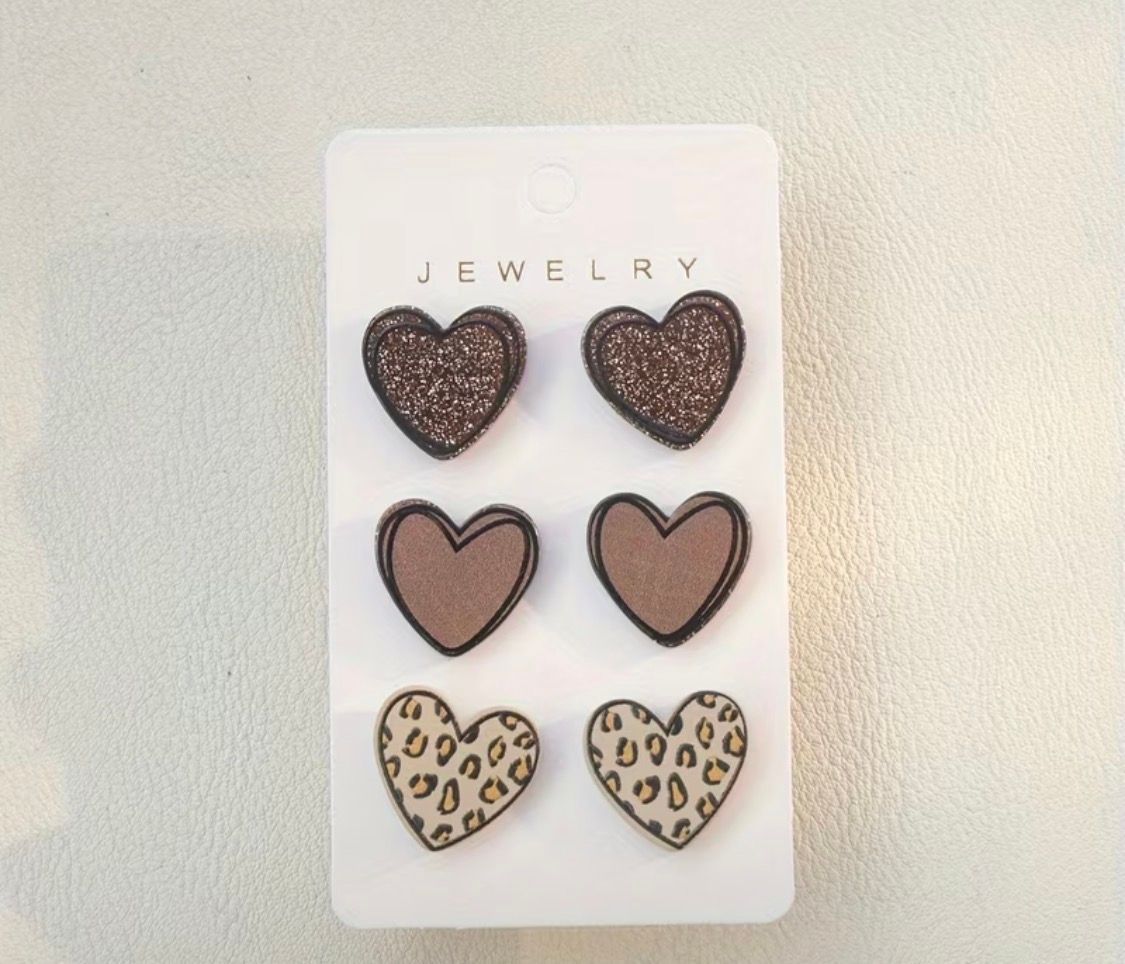Six heart-shaped earrings on a white jewelry card, in brown and leopard-print designs.