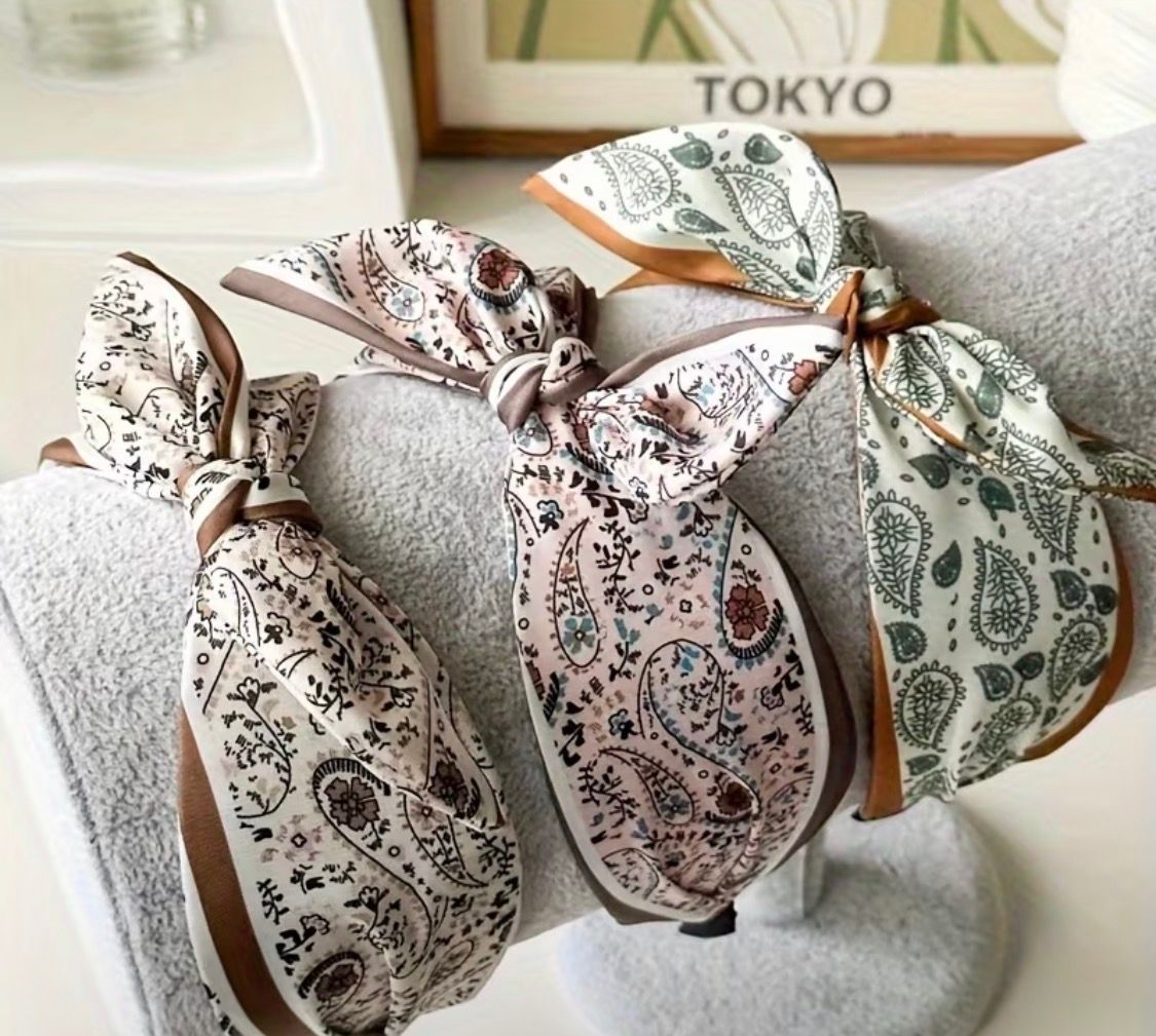 Patterned fabric scrunchies in beige, pink, and green arranged on display with a TOKYO sign behind them