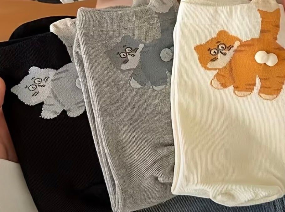 Three folded socks in black, cream, and gray with cat designs on a wooden table.