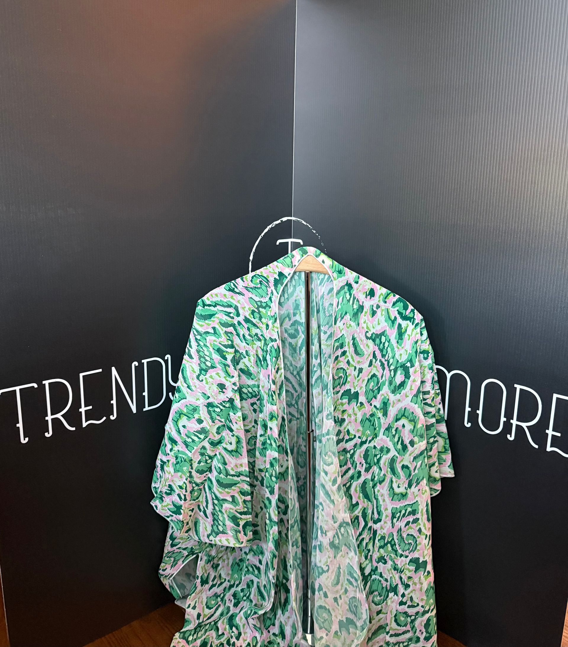 Floral green patterned dress hanging on a hanger against a black wall with partial chalk writing