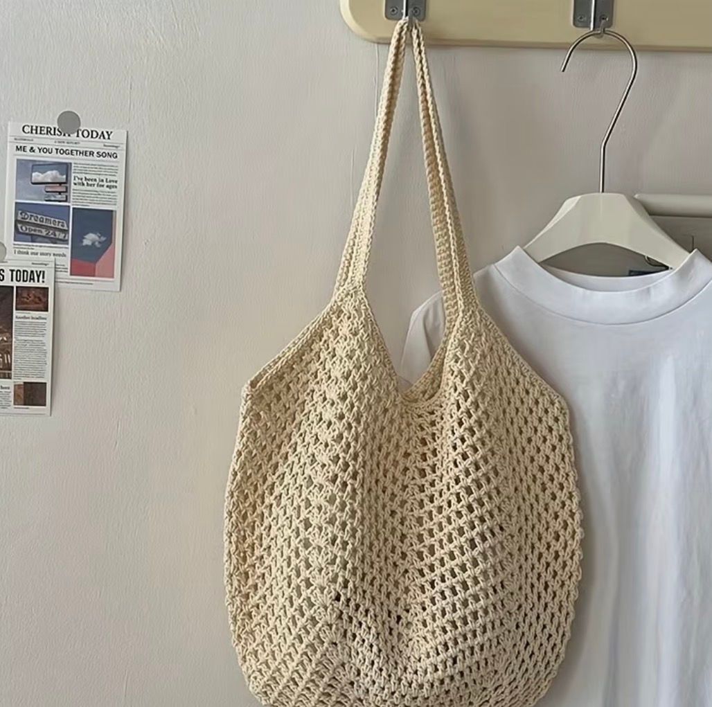 Three woven beach tote bags in cream, yellow, and tan on sandy shore by the ocean
