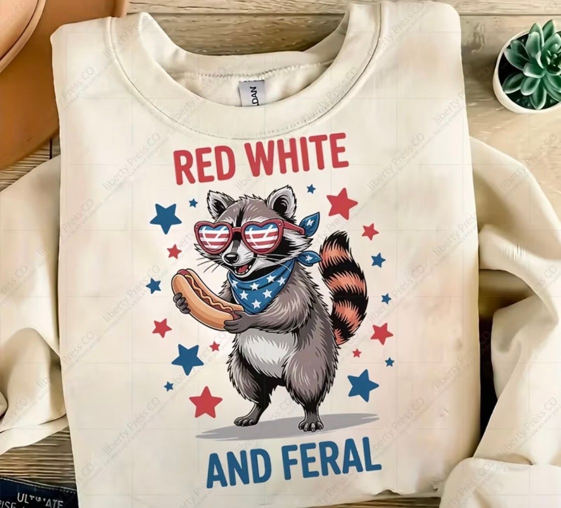 Cream sweatshirt with a raccoon wearing star sunglasses and patriotic text “RED WHITE AND FERAL”