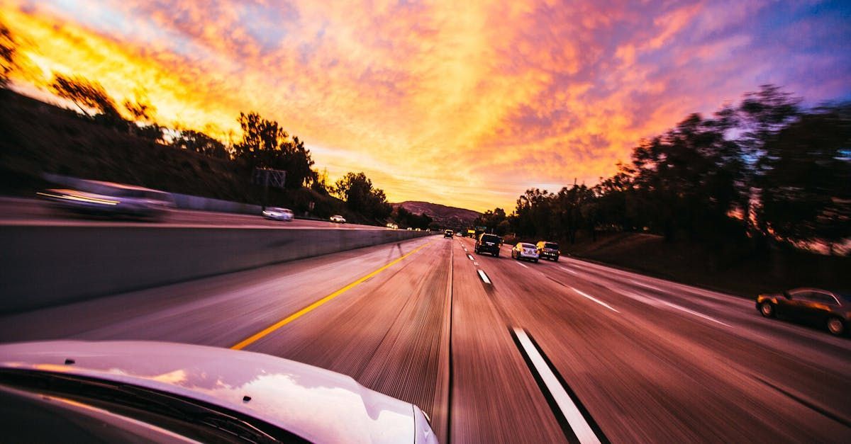 A car is driving down a highway at sunset.