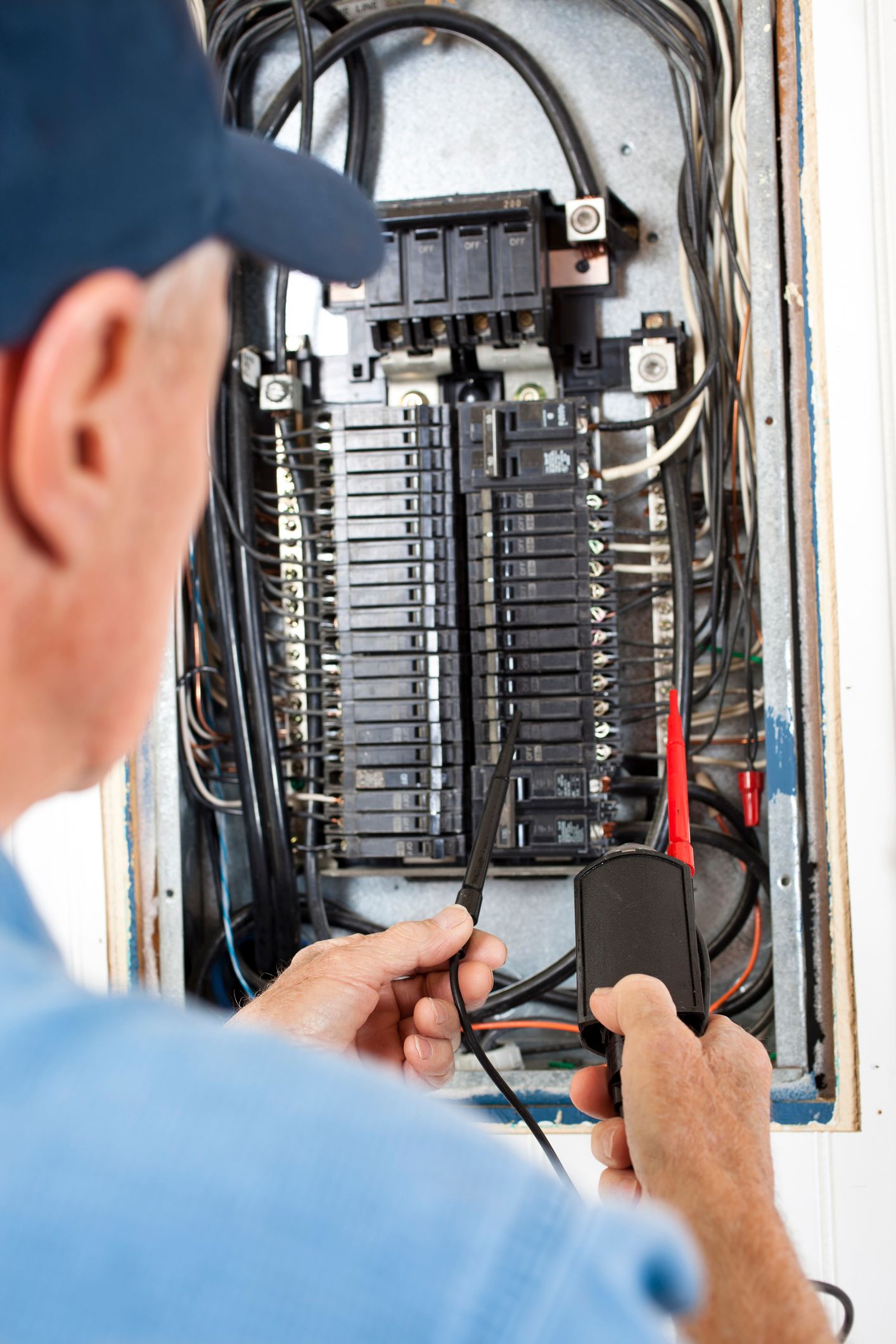 A man is working on an electrical box with a multimeter.