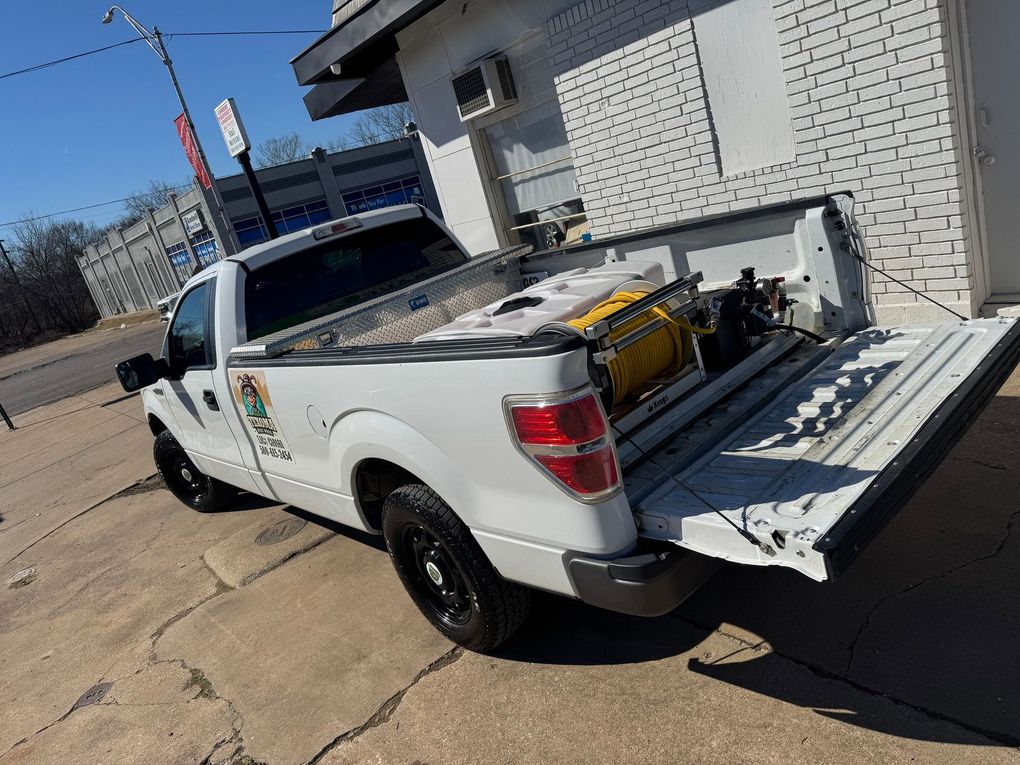 White pickup truck with rear cargo platform and equipment parked beside a building on a sunny street