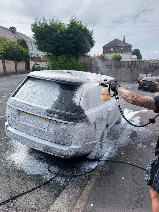 A silver range rover sport is parked in a driveway next to a white van.