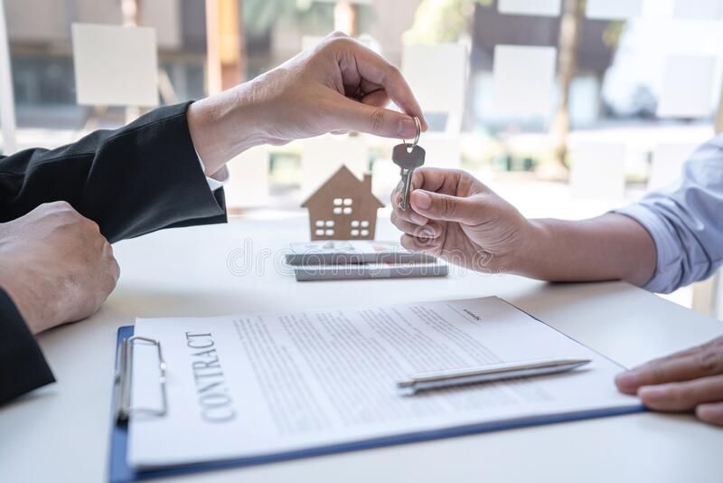 A person hands keys to another over a contract, representing a real estate transaction.