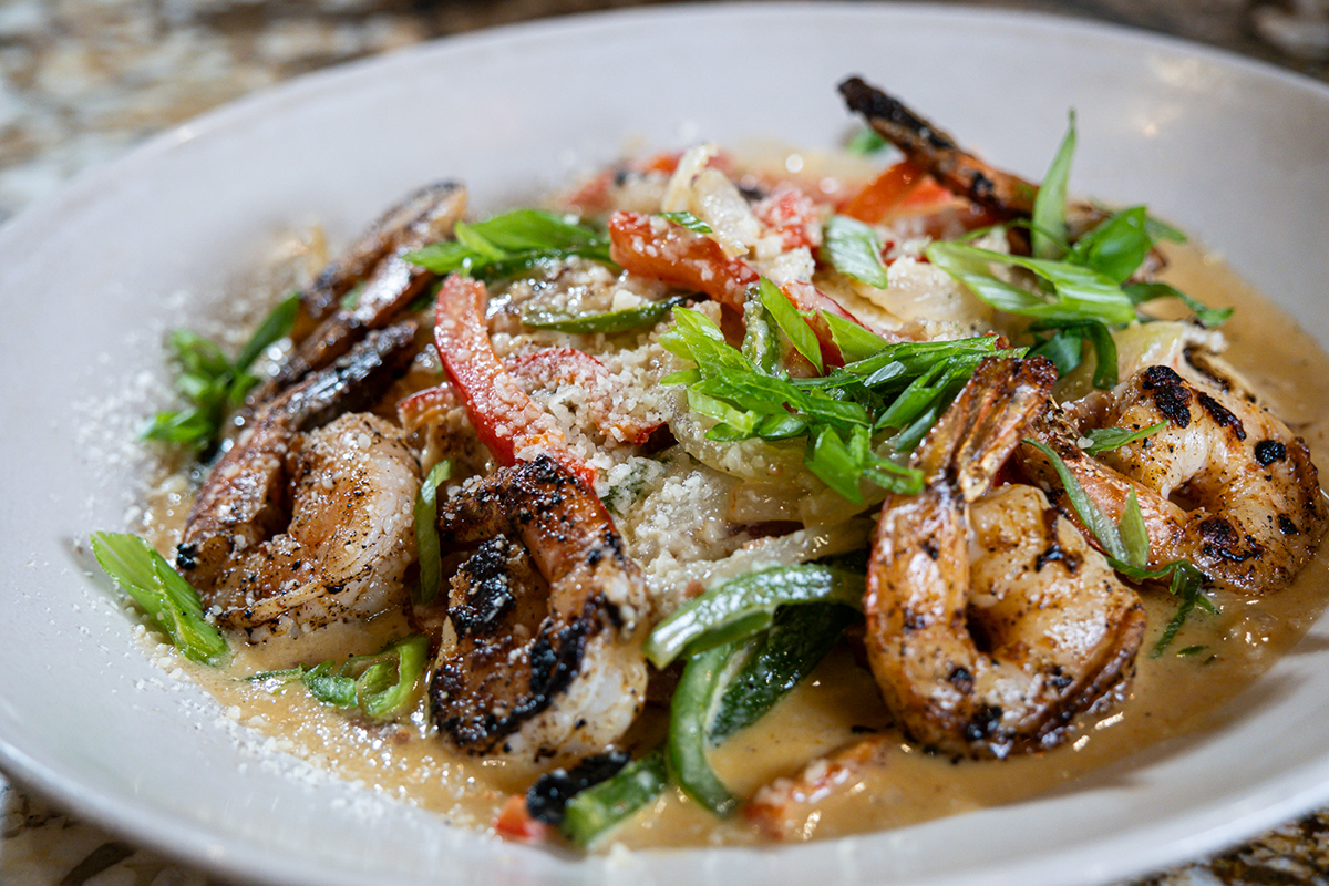 Grilled shrimp with vegetables and sauce in a white bowl, garnished with green onions.