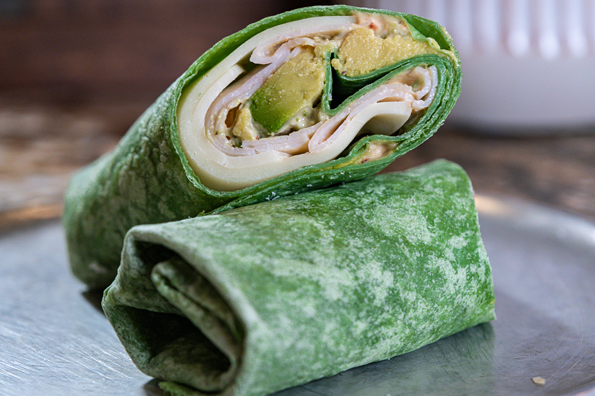 Green spinach wrap cut in half, filled with turkey, avocado, and sauce, resting on a silver plate.