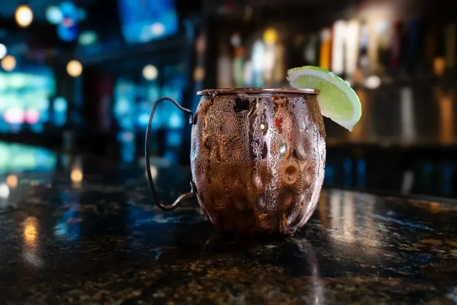 Copper mug with condensation and lime garnish on a bar. Blurred bar background with lights.