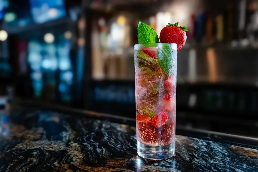 A refreshing strawberry mojito in a tall glass, garnished with a strawberry and mint sprig, sits on a bar.
