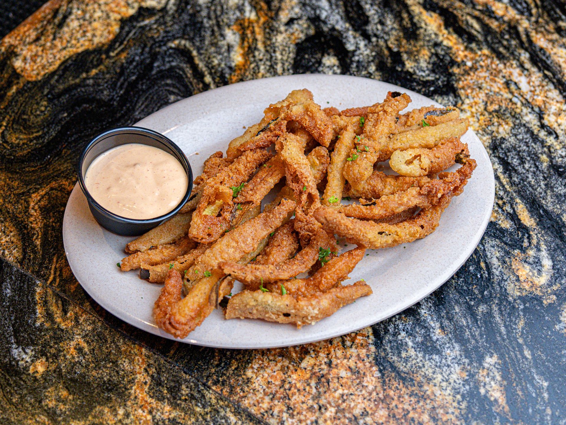 A plate of fried onion petals with dipping sauce on a table.