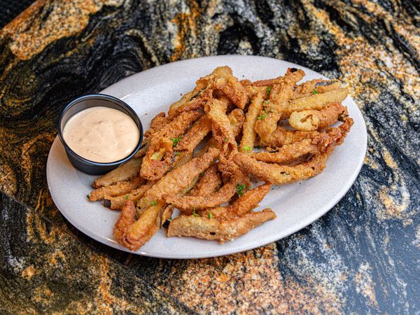 A plate of fried green beans with dipping sauce on a table.
