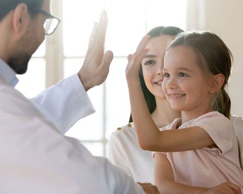 A doctor giving a high-five to a smiling child while a parent looks on in a bright, professional setting.