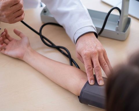 A medical professional measuring a patient's blood pressure with a cuff on their arm at a desk.