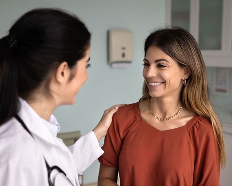 A professional with a stethoscope touches the shoulder of a smiling patient during a medical consultation.