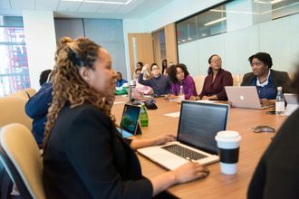 Team meeting around a conference table with laptops and coffee cups in a bright office room