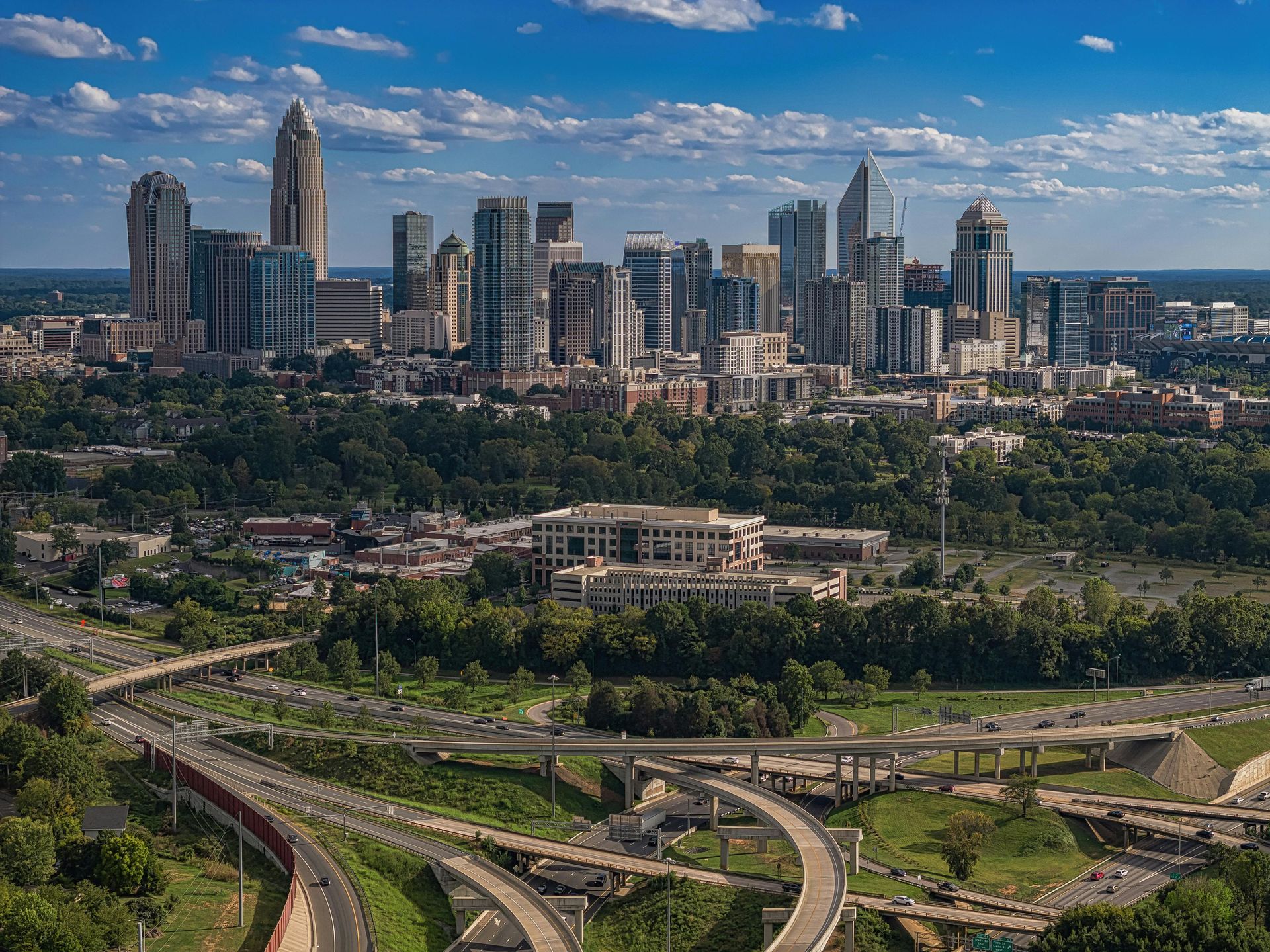 City skyline under a blue sky above green parkland and curving highways