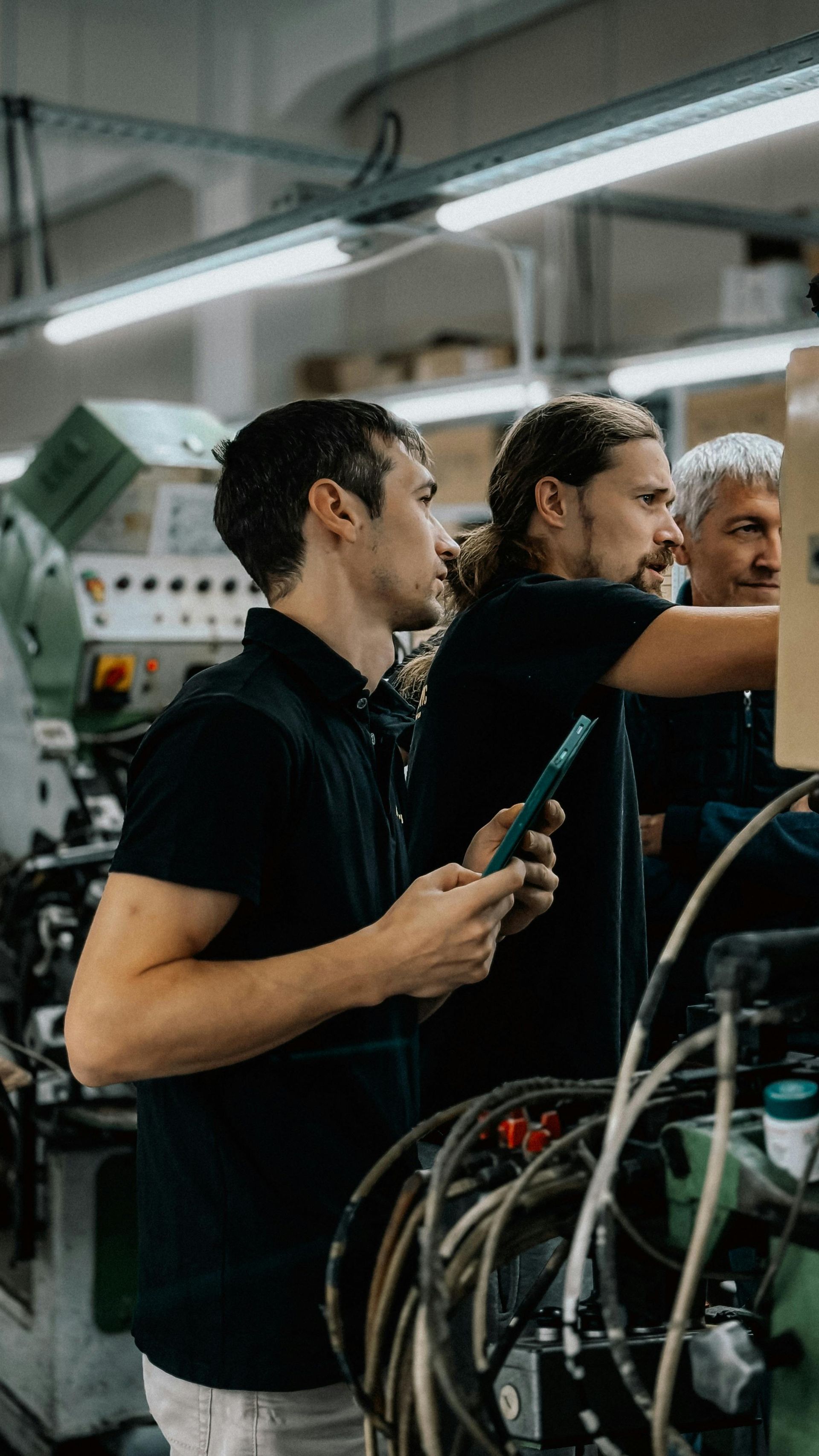 Two technicians working with wiring inside a factory beside industrial equipment