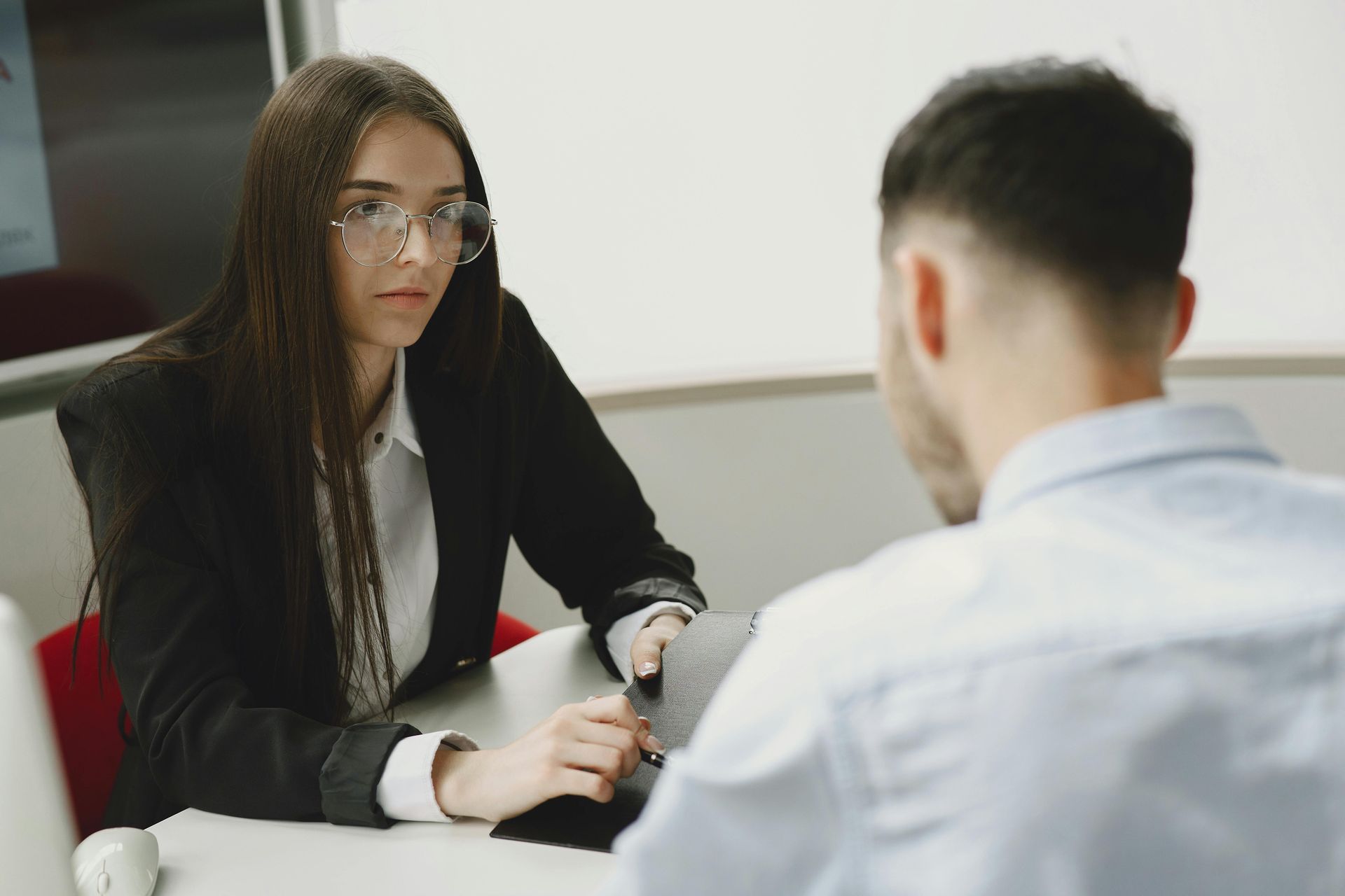 Two people in a meeting, one woman listening across a desk in an office setting
