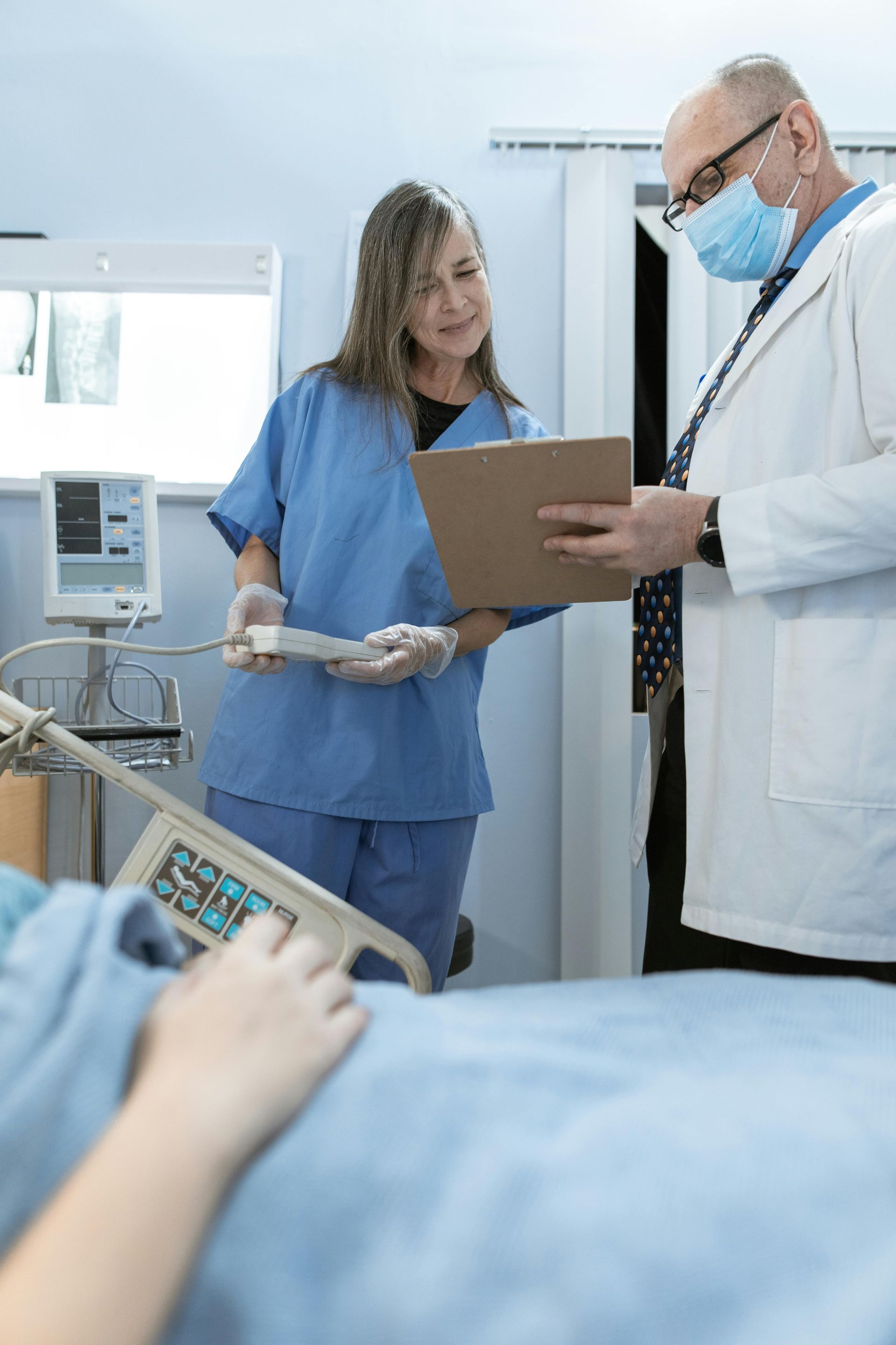 Medical staff reviewing a chart beside a hospital bed, with a patient in the foreground.