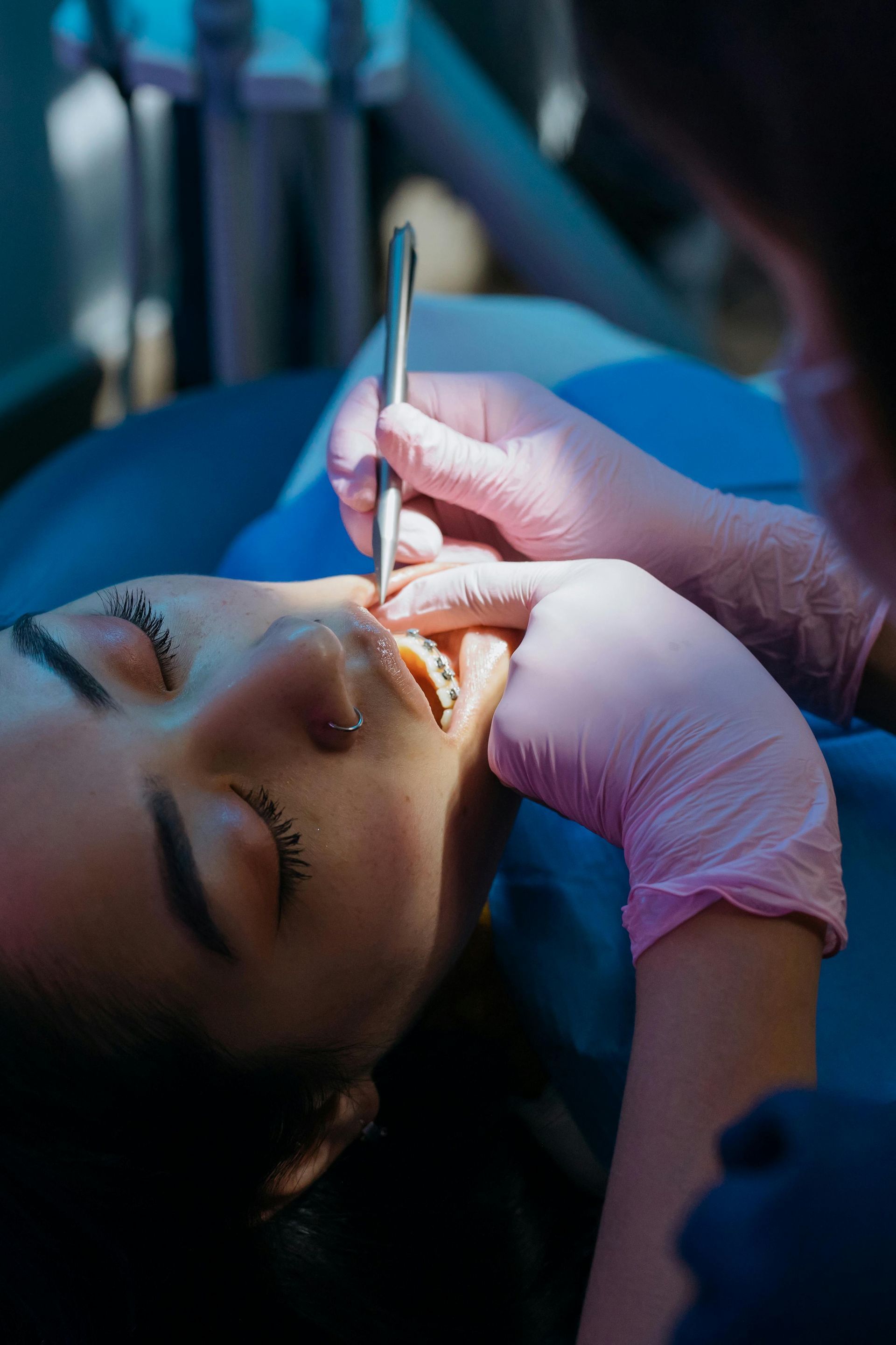 A person receives eyebrow treatment with a brush while lying down under blue lighting