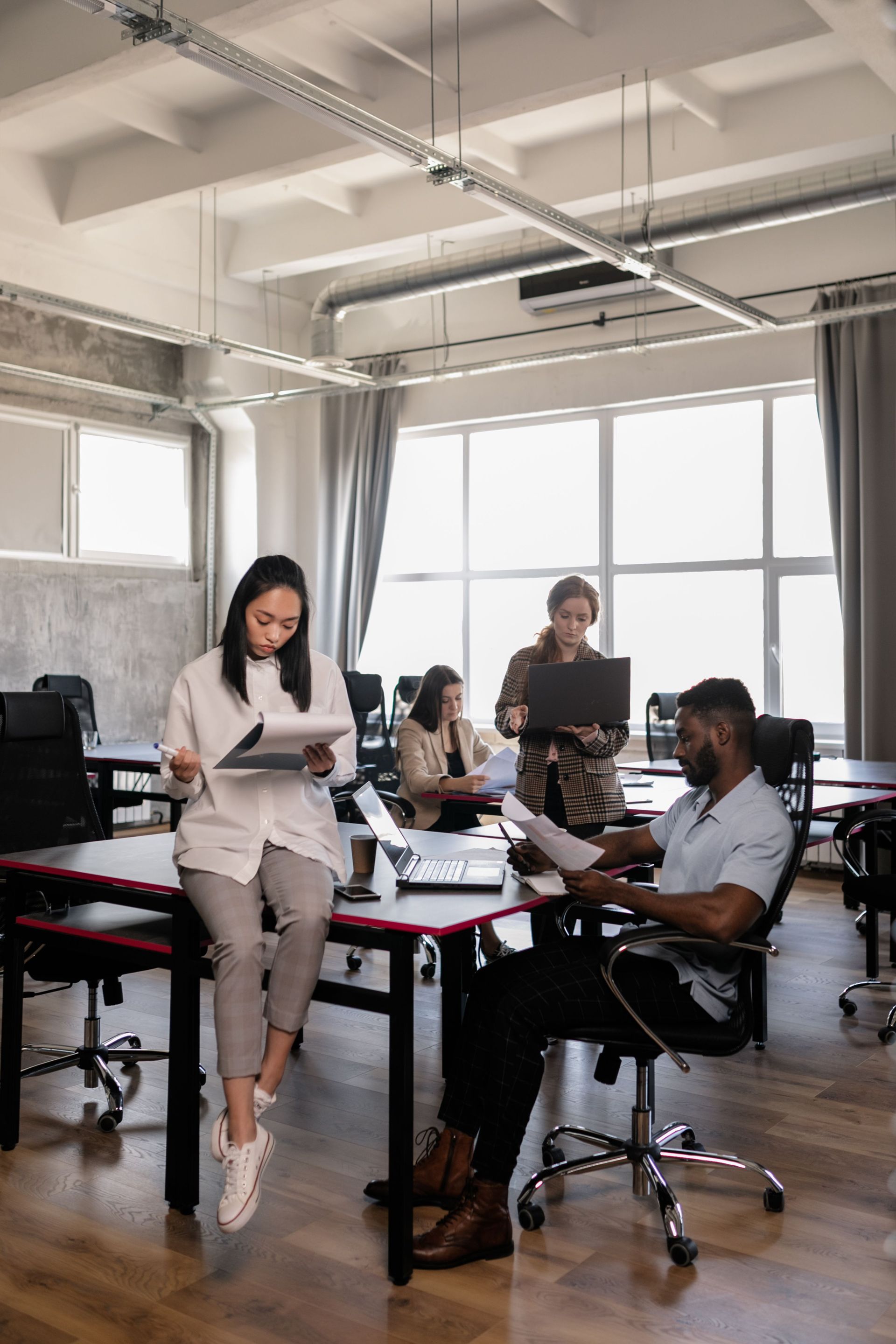 People working in a bright office with desks, computers, and large windows