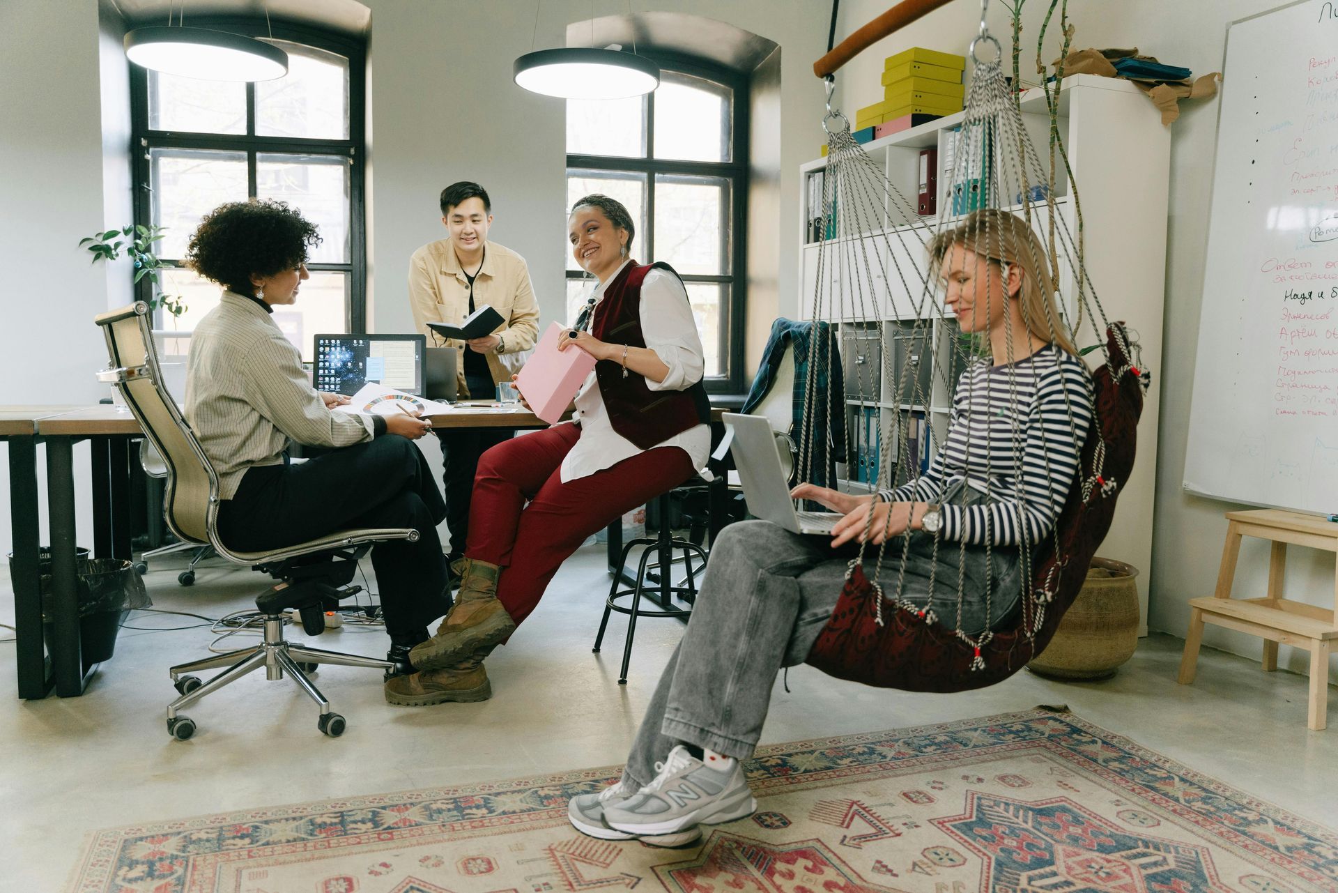 People gathered in a bright office, seated in chairs and chatting around a table.