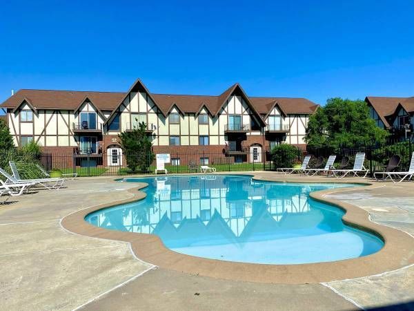 Pool in front of an apartment building with Tudor-style architecture under a clear blue sky.