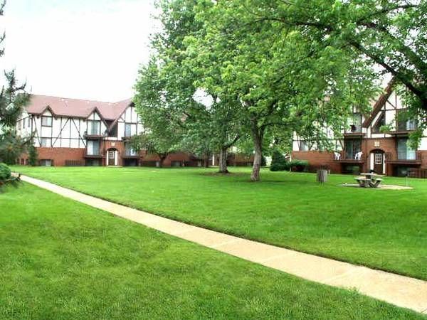 Green lawn with path leading to Tudor-style apartment buildings with brown roofs, trees.
