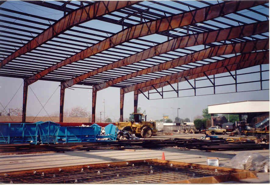 A partially constructed metal warehouse with blue equipment and a yellow loader on site.