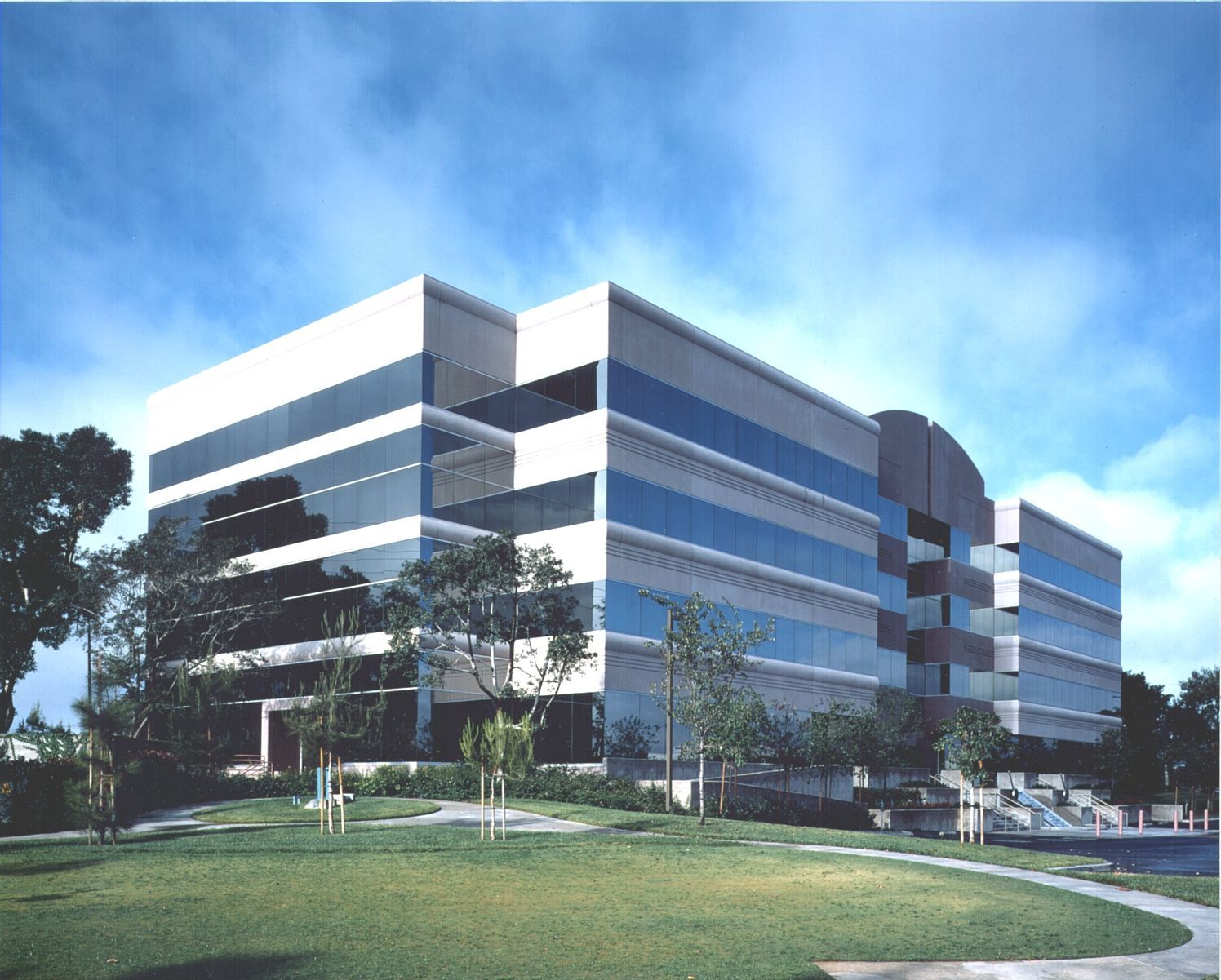 Modern office building with glass windows, green lawn, and blue sky.