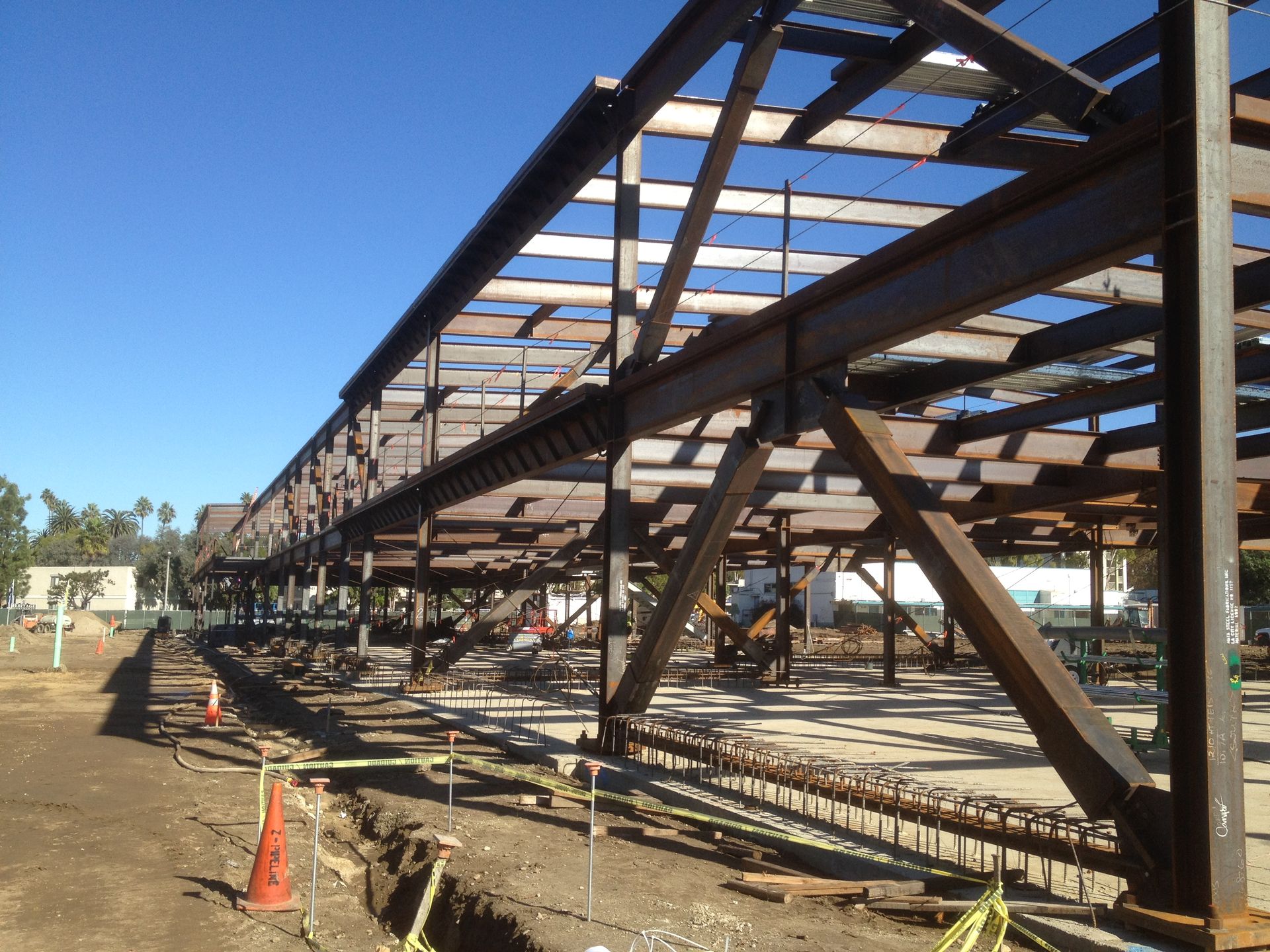 Steel framework of a building under construction, brown against a bright blue sky.