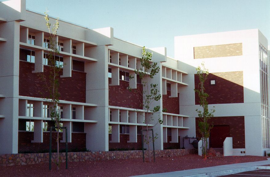 Two-story brick building with white columns and window grids, small trees in front, under a clear sky.