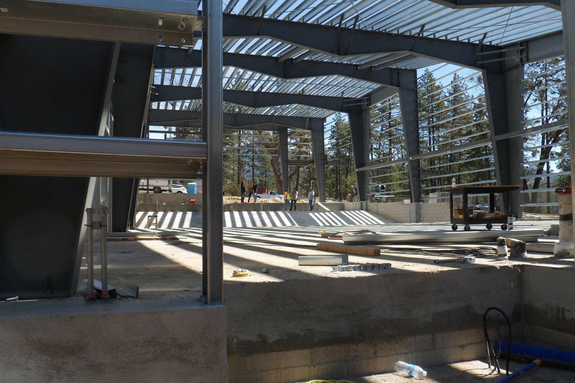 Steel framework of a building under construction, with a view of the surrounding trees and outdoors.