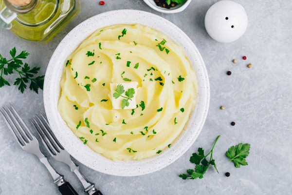 Mashed Potatoes with butter and fresh parsley in a white bowl on gray stone concrete background.