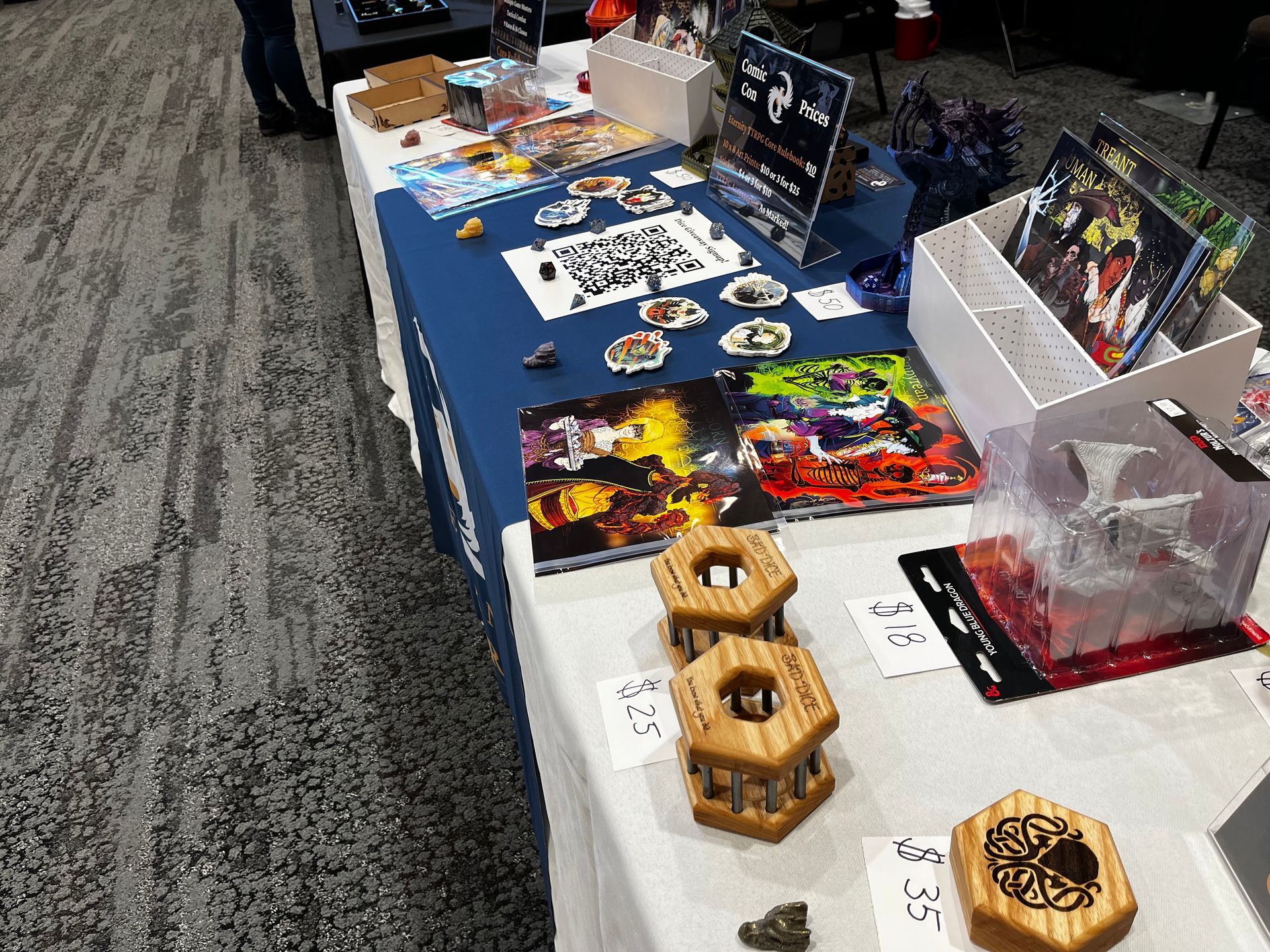 A table at a convention showcasing board games, dice, and art