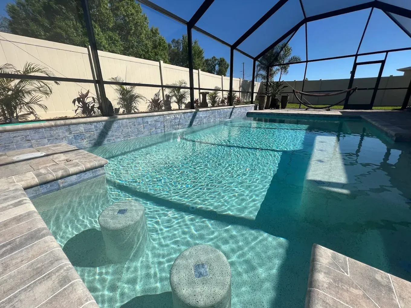 Swimming pool with built-in stools, blue water, screen enclosure, and surrounding stonework.