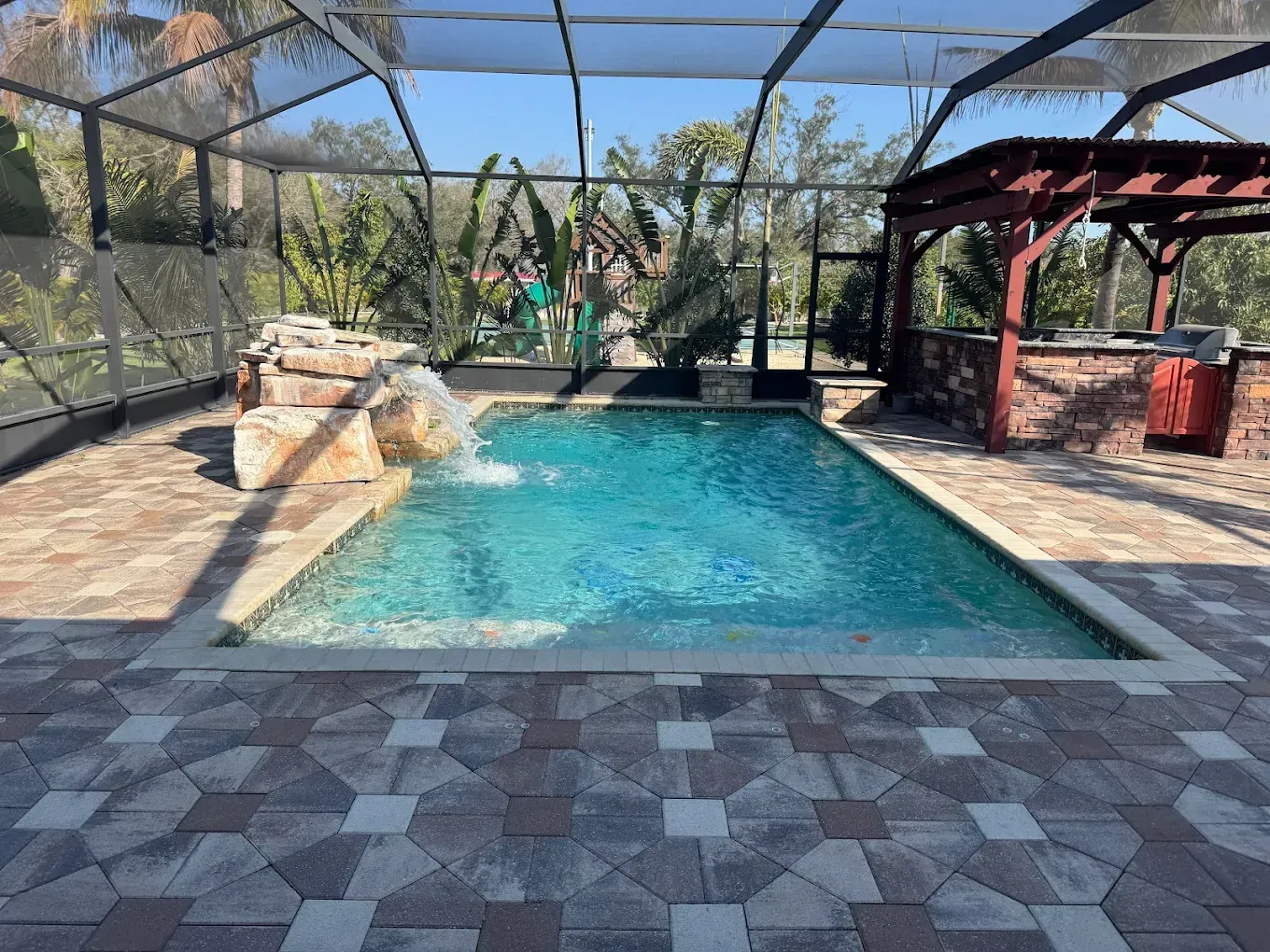 Pool enclosed by a screen. Waterfall feature, brick patio, and outdoor kitchen.