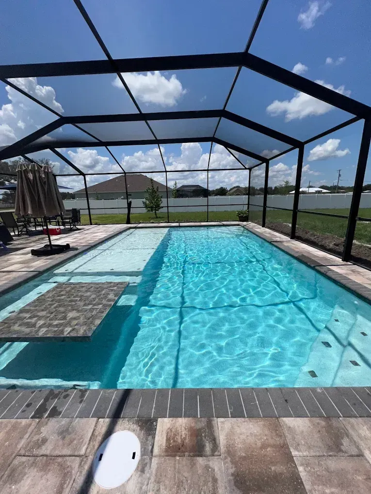 A rectangular pool with clear blue water under a black screened enclosure, surrounded by light-colored paving.