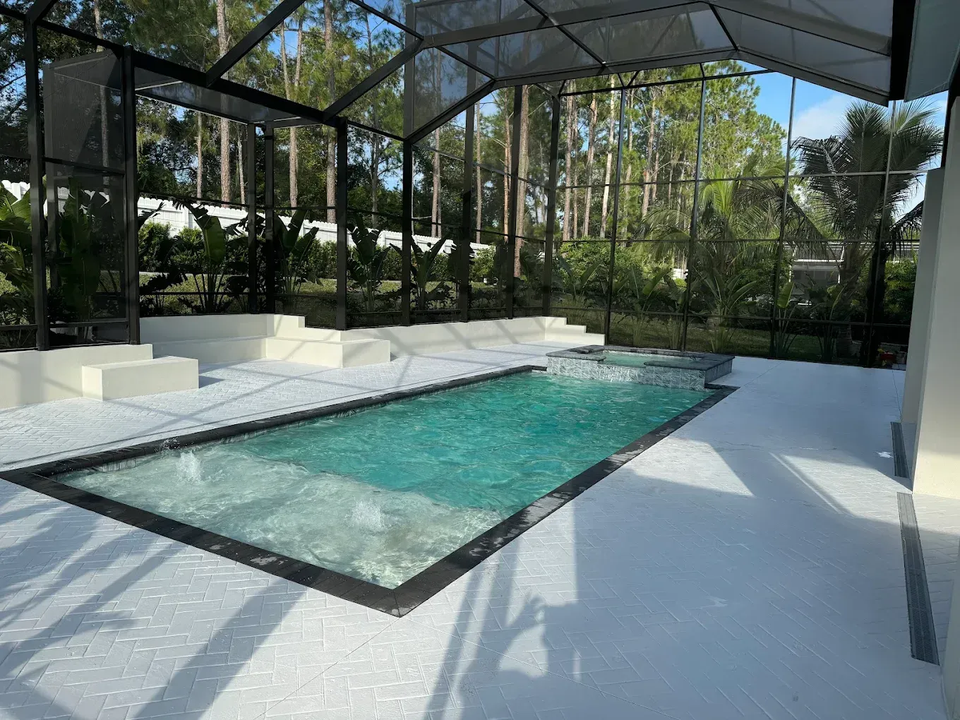 Pool enclosed in black screened structure; white deck and steps, trees in background.