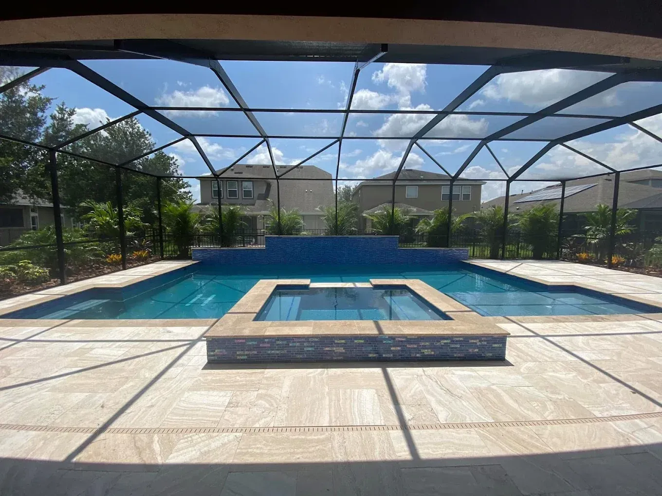 Swimming pool with screen enclosure, blue water, beige patio, sunny sky.
